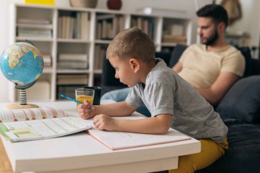 Baba, oğluyla evde ödev yapıyor.