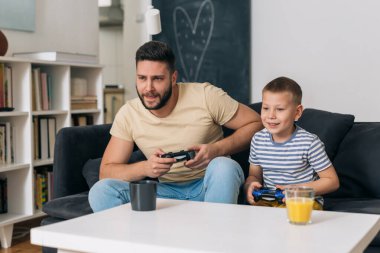Baba oğluyla evde video oyunu oynuyor.