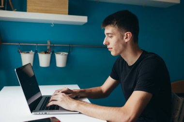 Öğrenci odasında masanın başında otururken dizüstü bilgisayar kullanıyor.