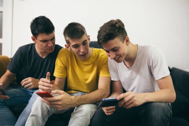 Arkadaşlar cep telefonu kullanıyor, evdeki kanepede oturuyor.