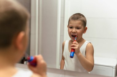 Genç bir çocuk banyoda dişlerini fırçalıyor.