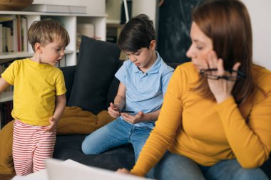 Annem evden laptopla çalışmaya çalışıyor. Çocukları arka planda oynuyor.