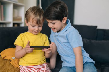 Çocuk evdeki koltukta otururken cep telefonu kullanıyor.