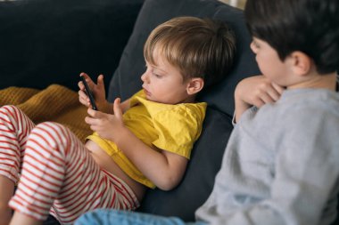 Çocuk evdeki koltukta otururken cep telefonu kullanıyor.