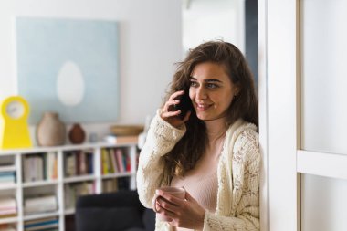 Kadın sabah kahvesini içiyor ve telefonda konuşuyor.