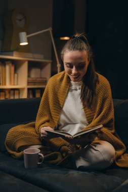 Kanepede dinlenen ve kitap okuyan bir kadın. Akşam karamsarlığı. Hafta sonu eğleniyor.