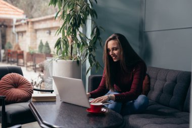 Evde dizüstü bilgisayarla çalışan bir kadın. Evdeki kanepede oturuyor.