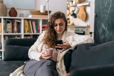 Kadın kanepede dinleniyor ve evde cep telefonu kullanıyor.