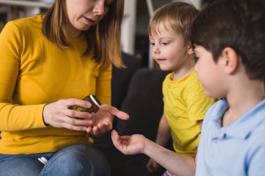 Anne, oğullarına vitamin hapı veriyor.