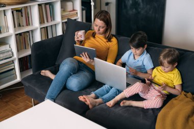 Anne oğullarıyla dizüstü bilgisayar kullanıyor. Evdeki kanepede oturuyorlar.