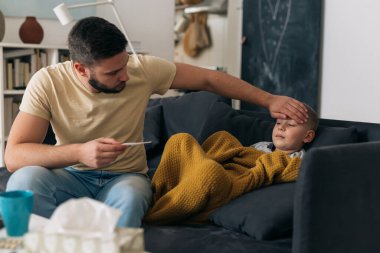Baba oğluna sıcaklık ölçer. Oğlanın bacası var.