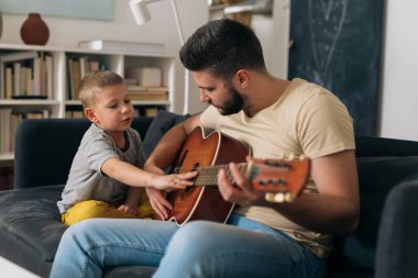 Baba ve oğul evde eğleniyorlar. Akustik gitar çalıyorlar.