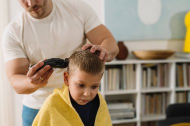 Baba evdeki oğluna saç kesiyor.