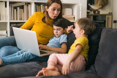 Anne çocuklarıyla dizüstü bilgisayar kullanıyor.