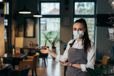 Yüzü maskeli garson restorana hoş geldin diyor.