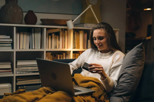 一个女人躺在沙发上 在家里用笔记本电脑上网购物 晚上的气氛 — 图库照片