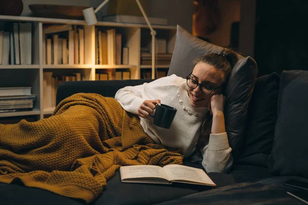 女人躺在沙发上 在家里看书 晚上的气氛 — 图库照片