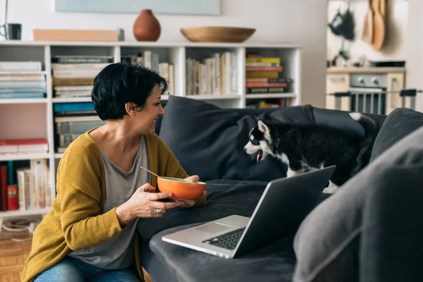 女人在家吃早餐 她正在用笔记本电脑 她的小狗在她身边 — 图库照片