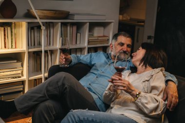 Orta yaşlı romantik çift evdeki kanepede otururken şarap içiyor.