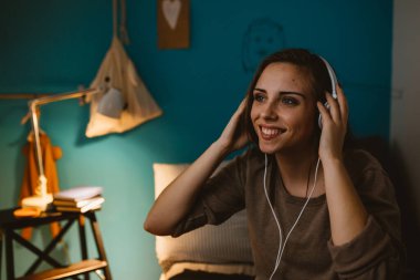 Kadın odasında dinleniyor ve kulaklıkla müzik dinliyor.