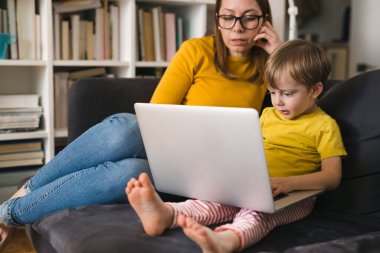 Anne ve çocuğu evde dizüstü bilgisayar kullanıyorlar.