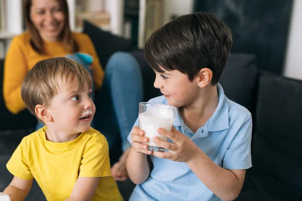 Çocuklar süt içiyor. Evdeki kanepede oturuyor.