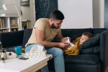 Baba oğlunun burnunu silmesine yardım eder. Çocuğun bacası var.