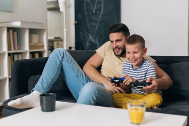 Baba oğluyla evde video oyunu oynuyor.