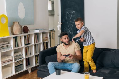 Baba oğluyla evde video oyunu oynuyor.