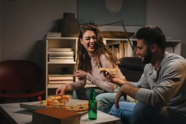 Öğrenciler evde pizza yerken eğleniyor.