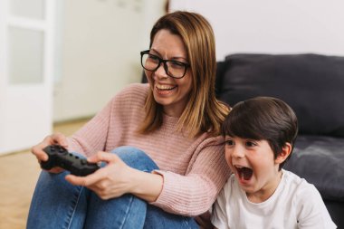 Anne ve oğlu evde video oyunu oynuyorlar.