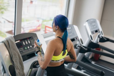 Dövmeli kadın spor salonunda çalışıyor. Koşu bandında koşuyor.