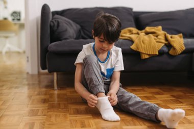 Çocuk yerde oturuyor ve evde çorap giyiyor.