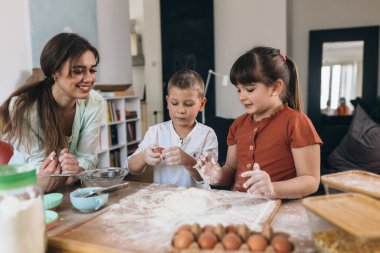 Anne ve çocuklar evde birlikte yemek pişiriyorlar.
