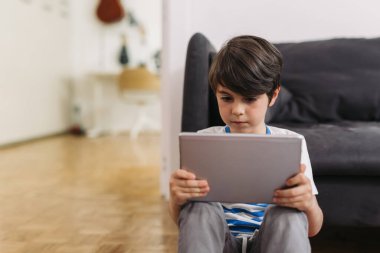 çocuk dijital tablet kullanıyor, evde yerde oturuyor.