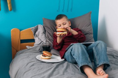 Hamburger yiyen ve odasında uzanan küçük bir çocuk.