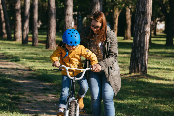 mother helping her son to ride a bike in public park