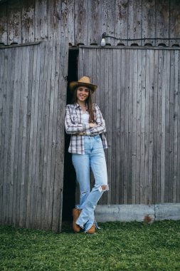 Çiftlik sahibi kadın ahırın önünde duruyor.