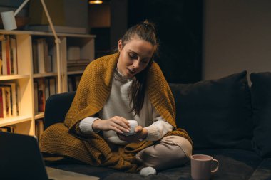 Kadın el kremi sürüyor, evde oturuyor.