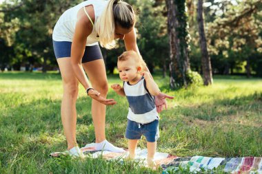 Genç anne, oğluyla birlikte parkta fiziksel egzersiz yapıyor.
