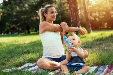 Genç anne, oğluyla birlikte parkta fiziksel egzersiz yapıyor.
