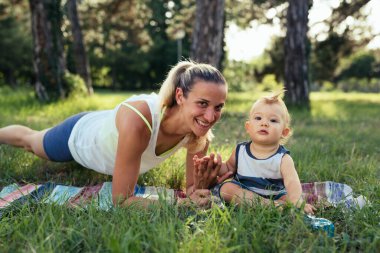 Genç anne, oğluyla birlikte parkta fiziksel egzersiz yapıyor.