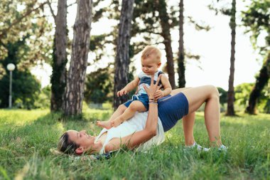 Genç anne, oğluyla birlikte parkta fiziksel egzersiz yapıyor.
