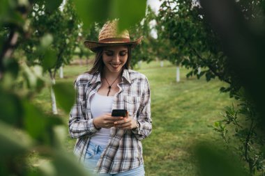 Kadın çiftçi meyve bahçesinde akıllı telefon kullanıyor.