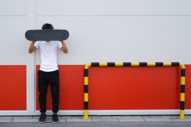 Kırmızı ve beyaz duvara karşı poz veren kaykaycı