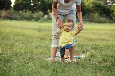 Anne ve oğlu halka açık bir parkta oynuyorlar. yürümeyi öğrenmek