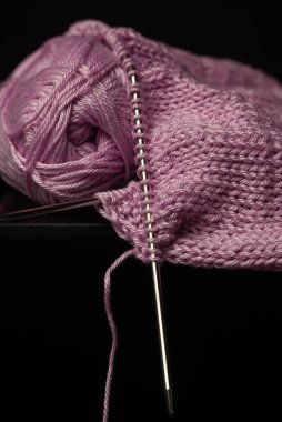 Siyah arka planda örgü iğneleri ve halkalarla pembe örülmüş kumaş.