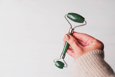 Kadın elinde yeşil kuvarstan yapılmış yeşil taş silindir, gua sha yüz masajı için doğal bir alet. Üst görünüm beyaz arkaplan, kopyala boşluk, kapat. Güzellik ve vücut bakımı.