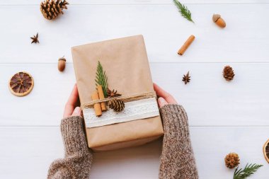 Dişi eller, doğal süslemelerle paketlenmiş şirin hediye kutusunu tutuyor. Sıfır Noel konsepti. Plastiksiz tatil. Sürdürülebilir yaşam tarzı.