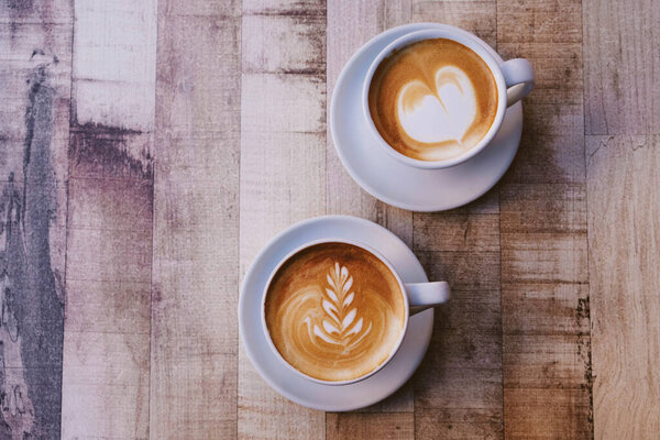 Two cups of fresh delicious cappuccino coffee with beautiful latte art on wooden background. From above, copy space.
